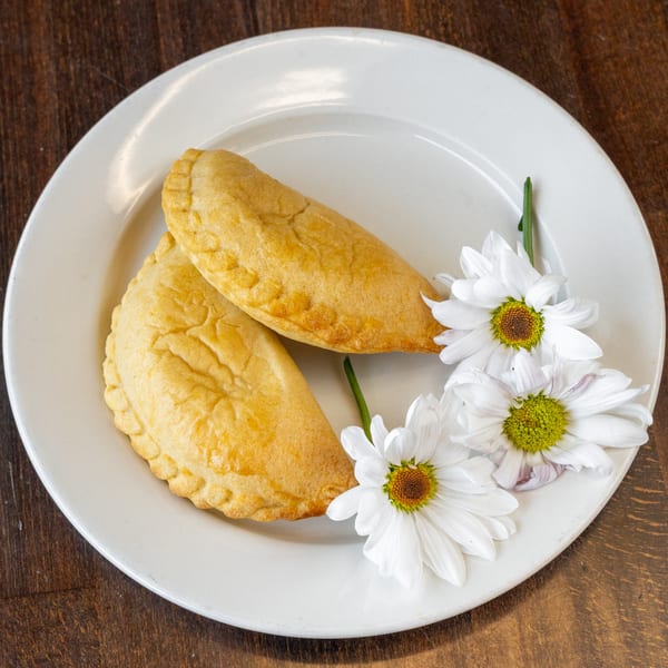 Two golden-brown Peruvian empanadas with crimped edges, garnished with white daisies on a white plate.