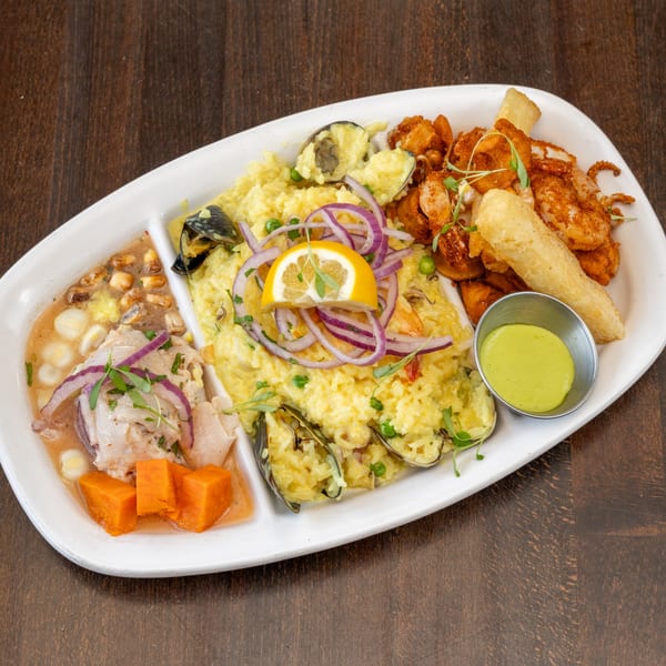 Peruvian seafood platter with ceviche, arroz con mariscos, fried seafood, and a green dipping sauce.