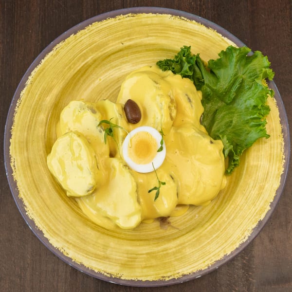 Peruvian Papa a la Huancaina with yellow sauce, hard-boiled egg, olive, and lettuce on a yellow plate.