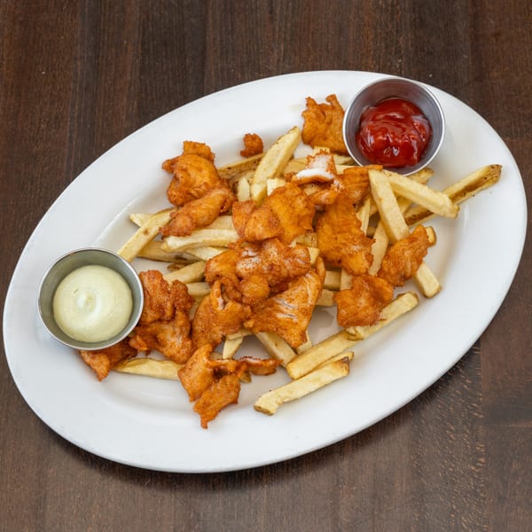 Peruvian fish and chips with ketchup and a creamy green sauce on a white oval plate.