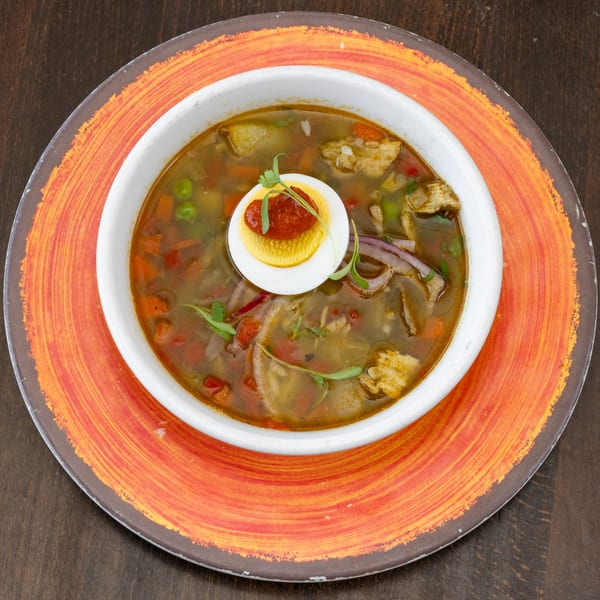 Peruvian chicken soup with vegetables, egg, and cilantro, served in a white bowl on an orange plate.