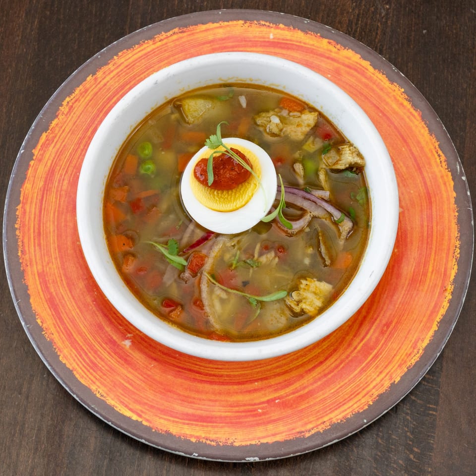 Peruvian chicken soup with vegetables, egg, and cilantro, served in a white bowl on an orange plate.