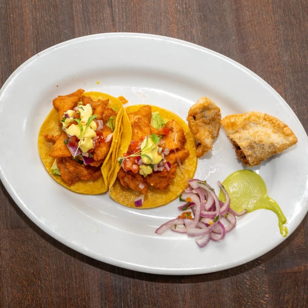 Two Peruvian fish tacos with avocado, pico de gallo, and a side of fried empanadas and red onions.