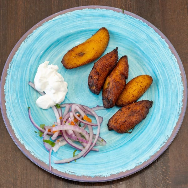 Fried plantains, red onion, and white sauce on a blue plate at Sazon Peruvian Cuisine.